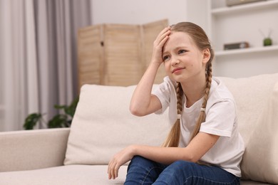 Photo of Little girl suffering from headache on sofa indoors