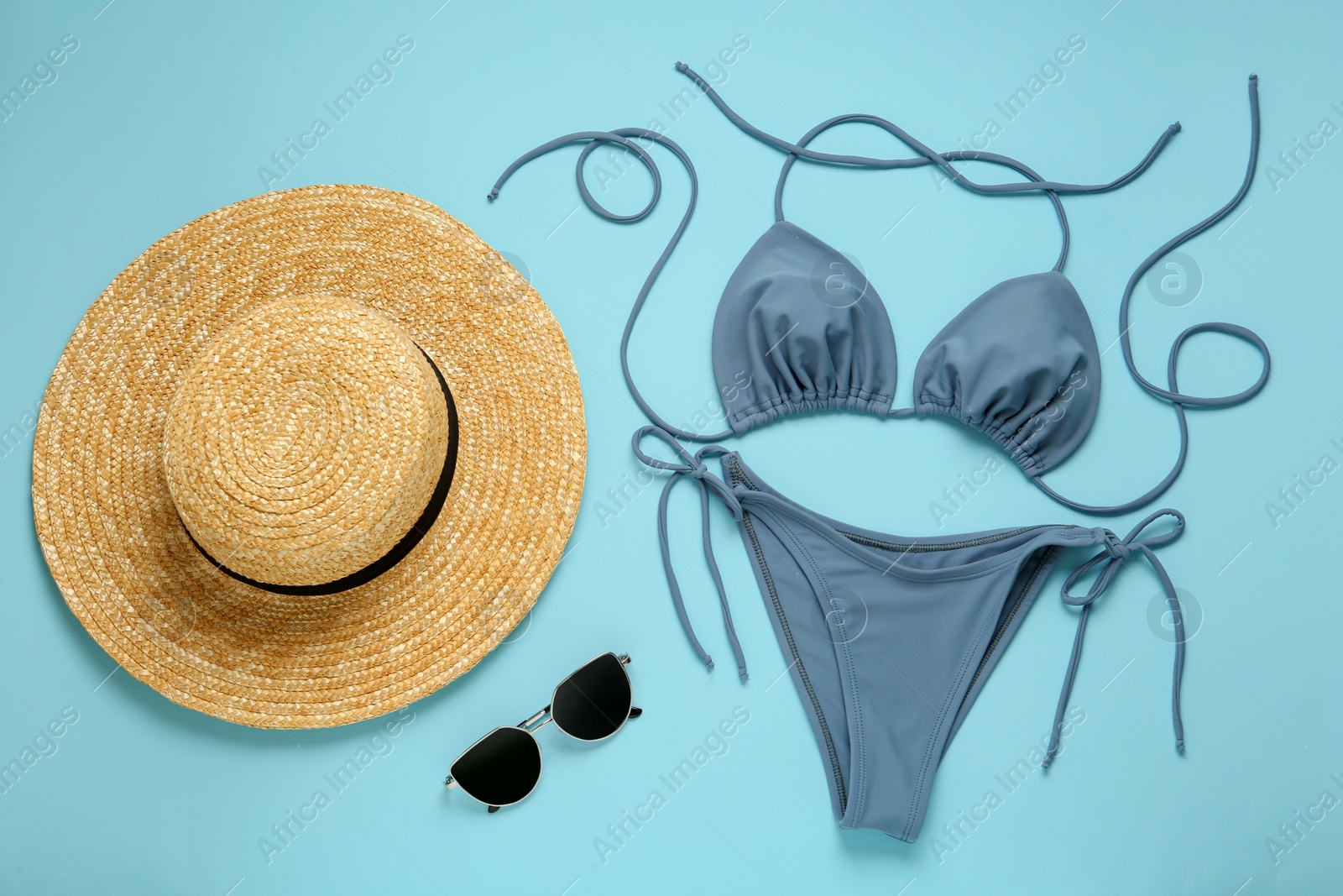 Photo of Stylish bikini, sunglasses and hat on light blue background, flat lay