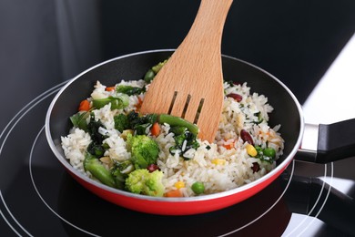 Photo of Frying tasty rice with vegetables on induction stove in kitchen, closeup