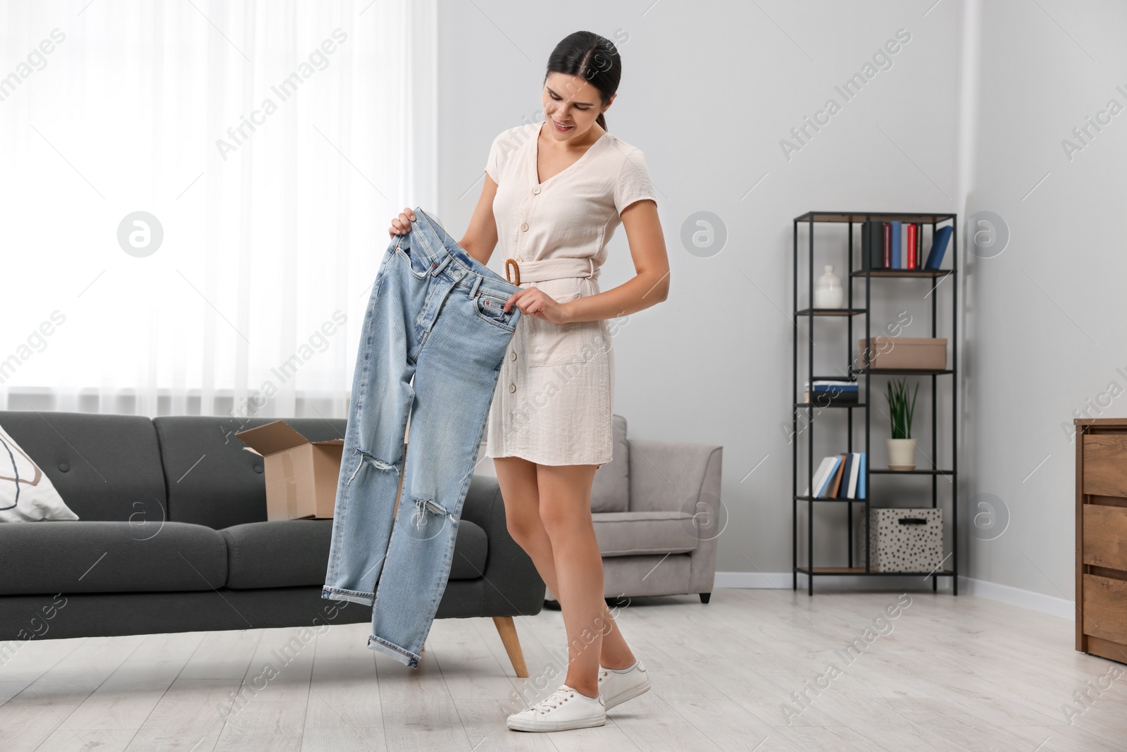 Photo of Young woman with just unpacked new jeans at home. Online shopping