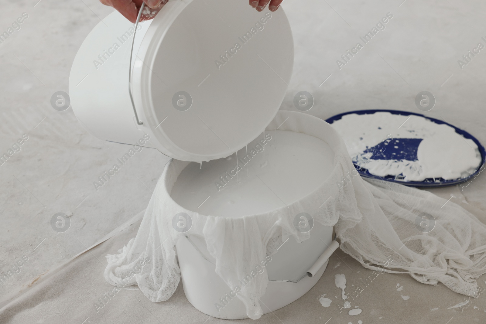 Photo of Decorator filtering paint in bucket on white floor, closeup