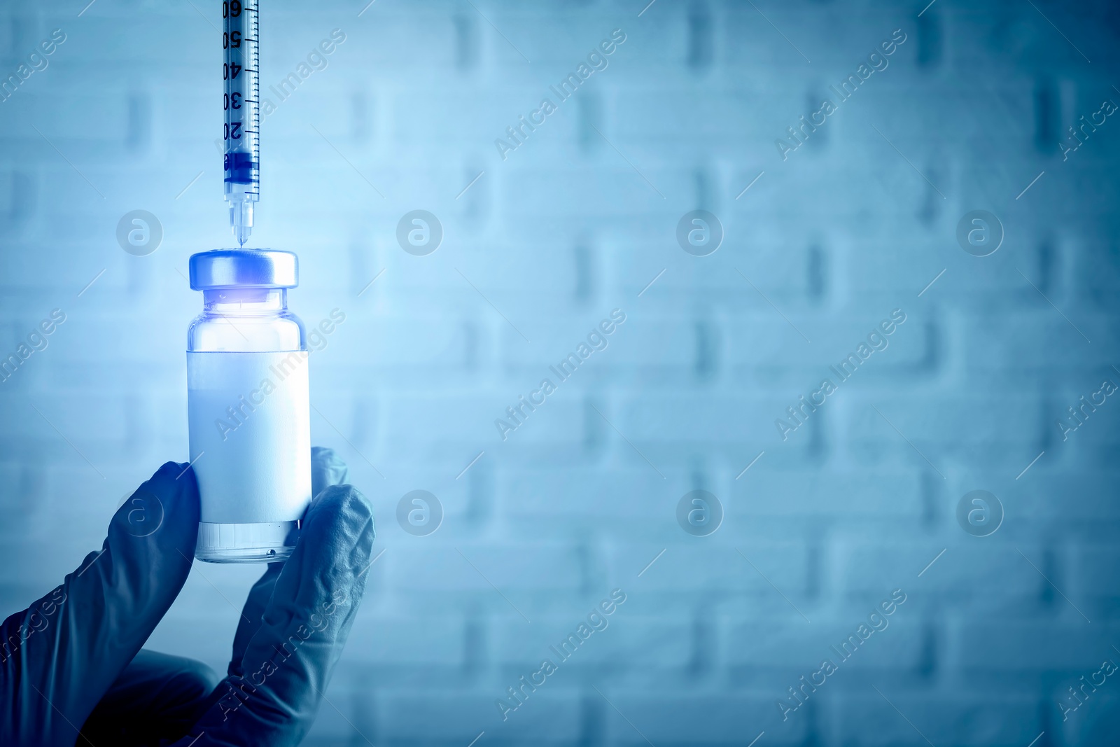 Image of Laboratory worker filling syringe with medication from vial near white brick wall, closeup with space for text. Color toned