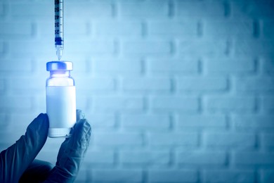 Laboratory worker filling syringe with medication from vial near white brick wall, closeup with space for text. Color toned