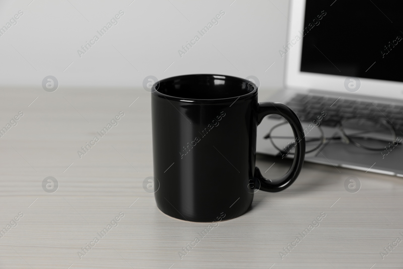 Black ceramic mug, laptop and glasses on white wooden table at workspace Photo of Black ceramic mug, laptop and glasses on white wooden table at workspace