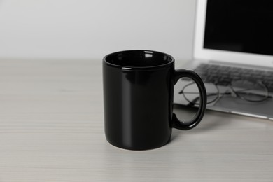 Photo of Black ceramic mug, laptop and glasses on white wooden table at workspace