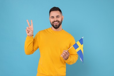 Photo of Young man holding flag of Sweden on light blue background
