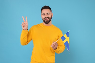 Young man holding flag of Sweden on light blue background