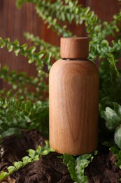 Photo of Wooden bottle of cosmetic product and green leaves on table, closeup