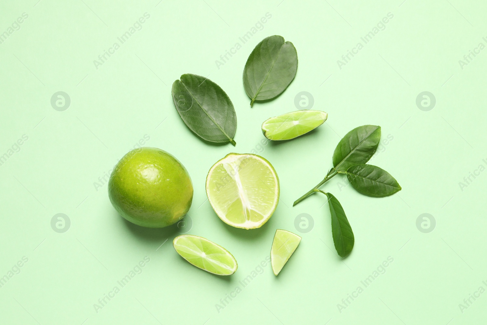 Photo of Whole and cut fresh ripe limes with leaves on light green background, flat lay