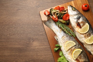 Photo of Delicious baked fish and vegetables on wooden table, top view. Space for text