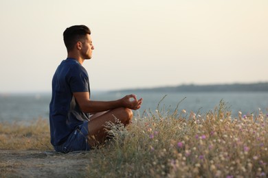 Man meditating near river on sunny day, space for text