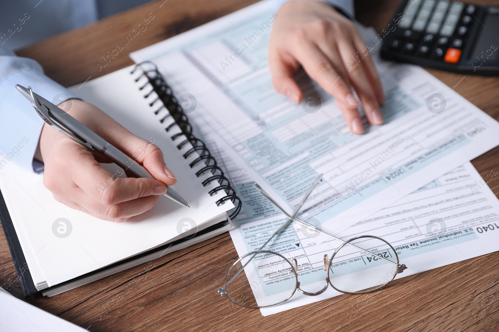 Photo of Payroll. Woman taking notes in notebook while working with tax return forms at wooden table, closeup