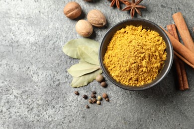 Photo of Dry curry powder in bowl and other spices on dark textured table, flat lay. Space for text