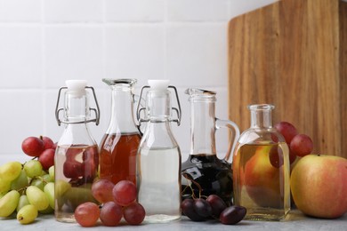 Photo of Different types of vinegar and fresh fruits on grey table