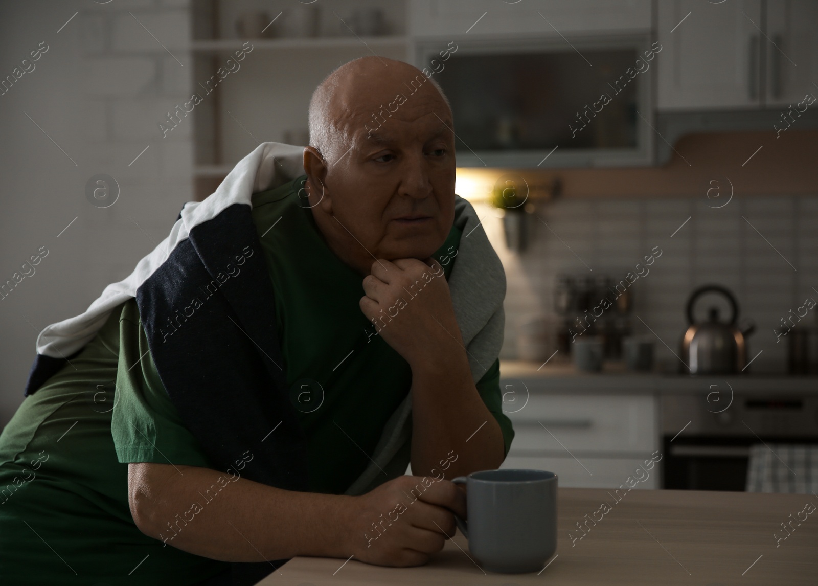 Photo of Elderly man with cup of tea at table in kitchen