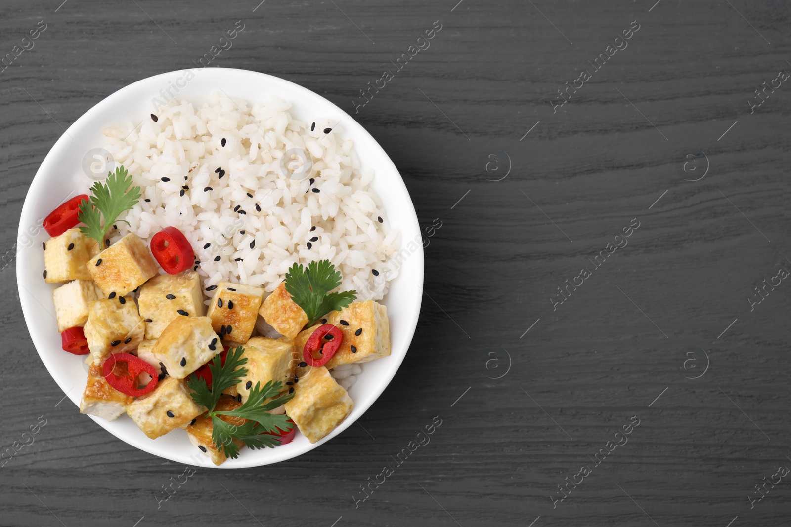 Photo of Bowl of rice with fried tofu, chili pepper and parsley on grey wooden table, top view. Space for text