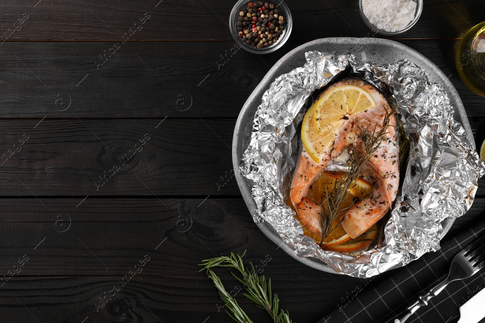 Photo of Tasty salmon baked in foil with lemon, spices and rosemary on dark wooden table, flat lay. Space for text