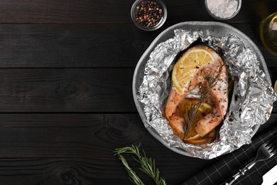 Tasty salmon baked in foil with lemon, spices and rosemary on dark wooden table, flat lay. Space for text