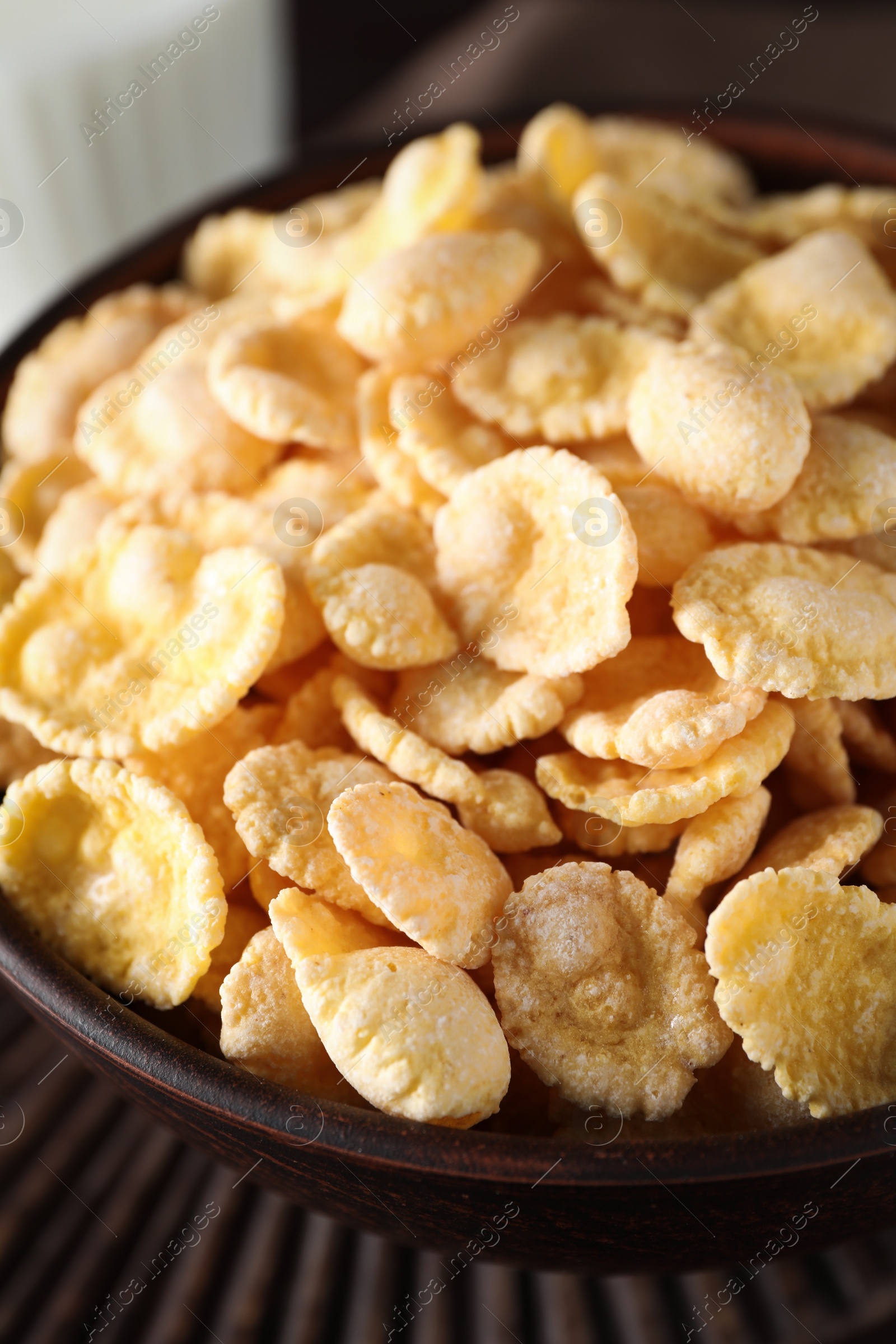 Photo of Bowl of tasty crispy corn flakes on wooden board, closeup