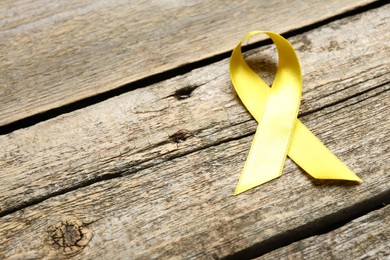 Photo of Yellow awareness ribbon on wooden table, above view. Space for text