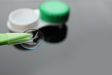 Tweezers with contact lens on blurred background, closeup. Space for text
