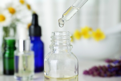 Dropping essential oil into bottle on blurred background, closeup