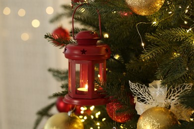 Photo of Christmas lantern with burning candle on fir tree against blurred background, closeup