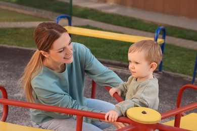 Photo of Happy nanny and cute little boy on carousel outdoors