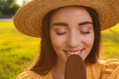 Photo of Beautiful young woman eating ice cream glazed in chocolate outdoors, closeup