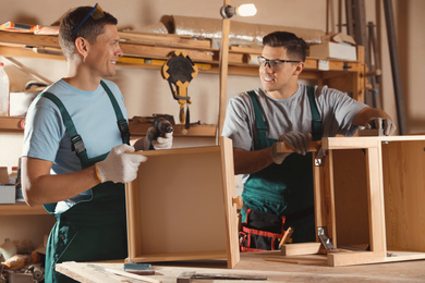 Professional carpenters assembling wooden cabinet in workshop