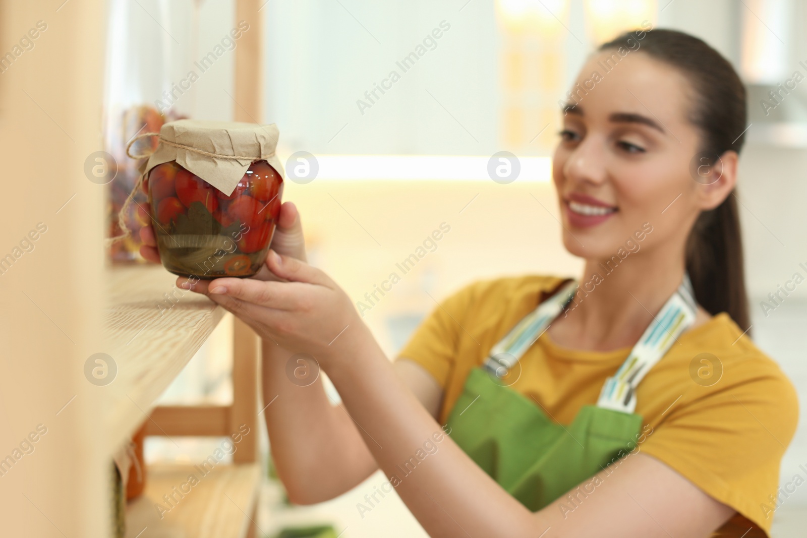 Photo of Woman putting jar of pickled vegetables on shelf indoors