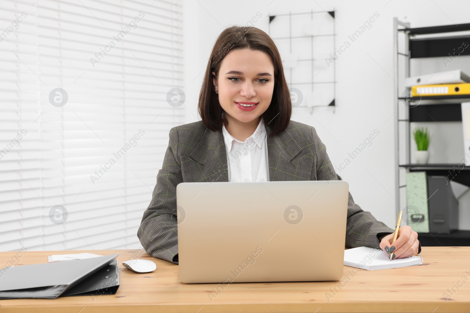 Photo of Happy young intern working with laptop at table in modern office