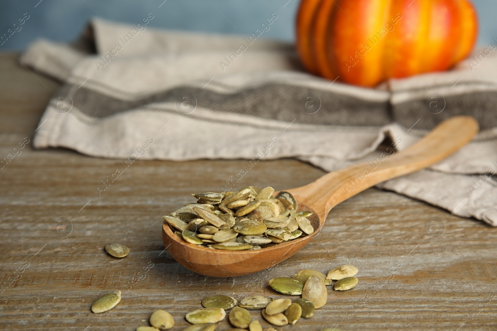 Photo of Spoon of raw peeled pumpkin seeds on wooden table. Space for text