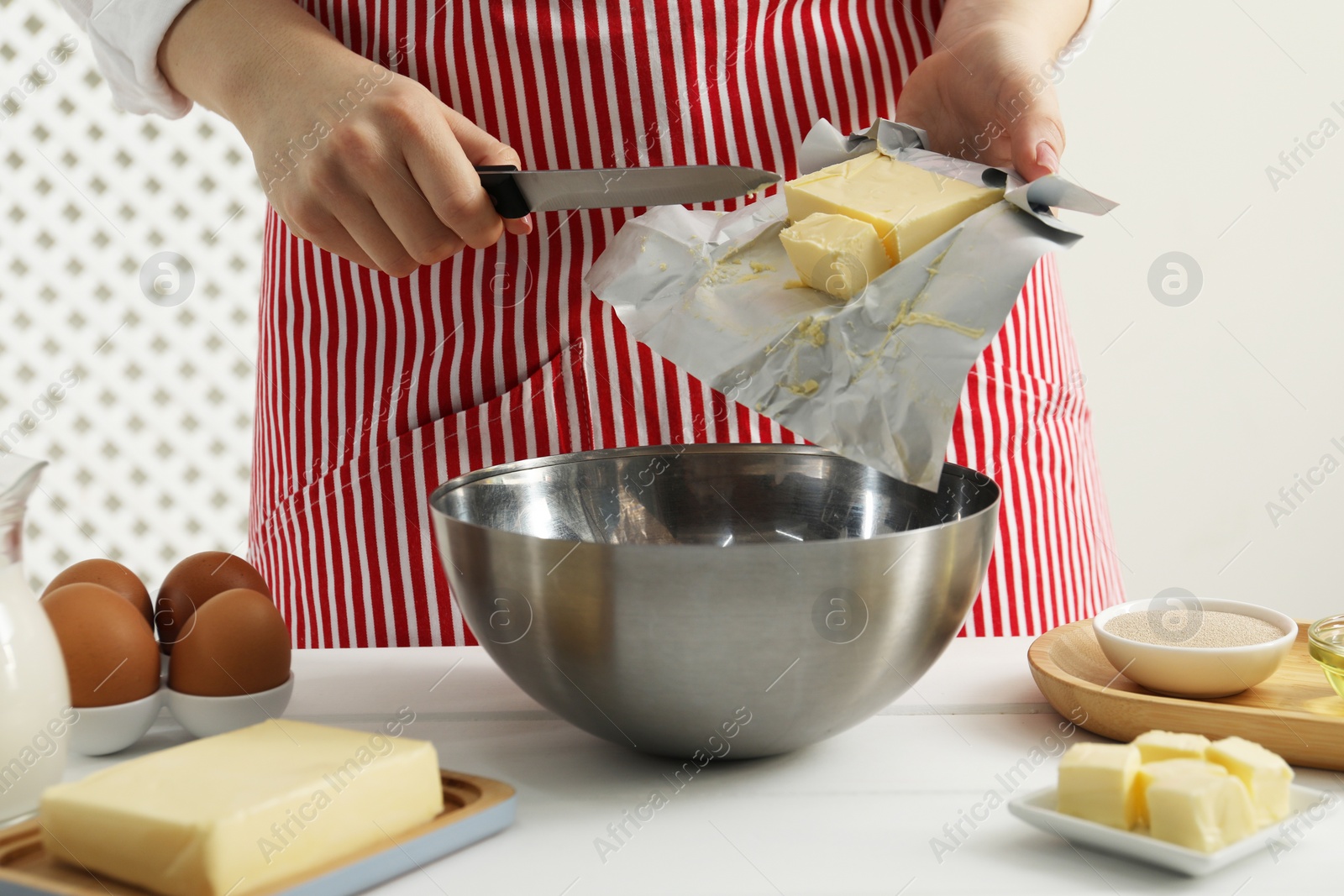 Photo of Woman adding fresh butter into bowl at white wooden table, closeup