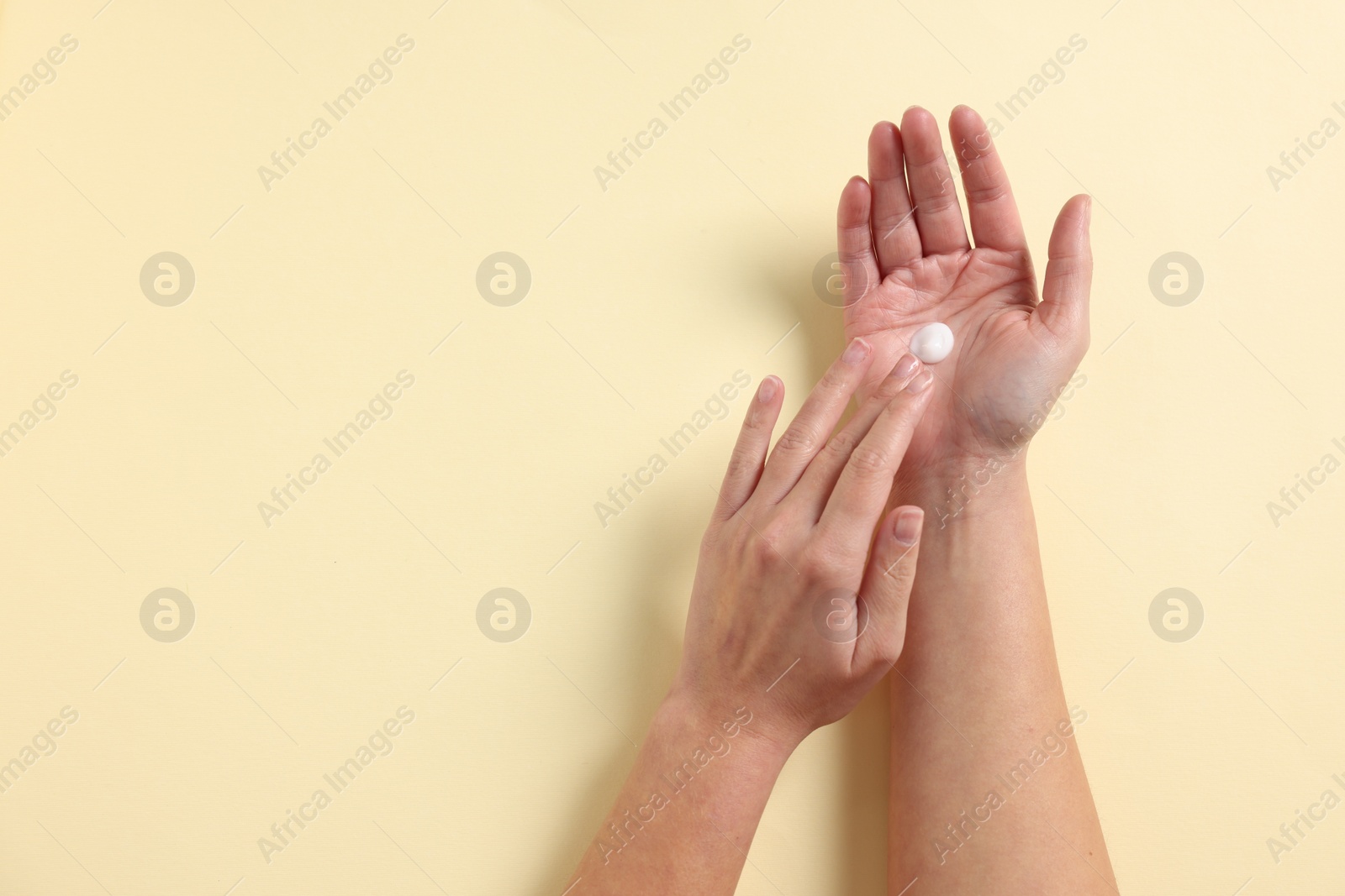 Photo of Woman applying cosmetic cream onto hand on beige background, above view. Space for text