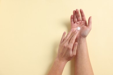 Woman applying cosmetic cream onto hand on beige background, above view. Space for text