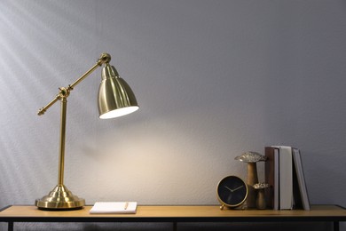 Stylish lamp, clock and books on wooden table indoors. Interior design
