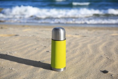 Yellow thermos with hot drink on sand near sea