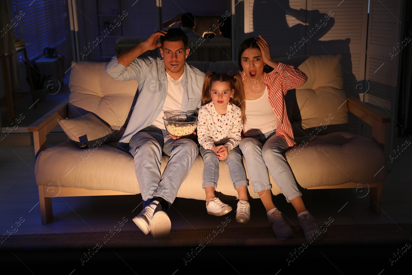 Photo of Family watching movie with popcorn on sofa at night