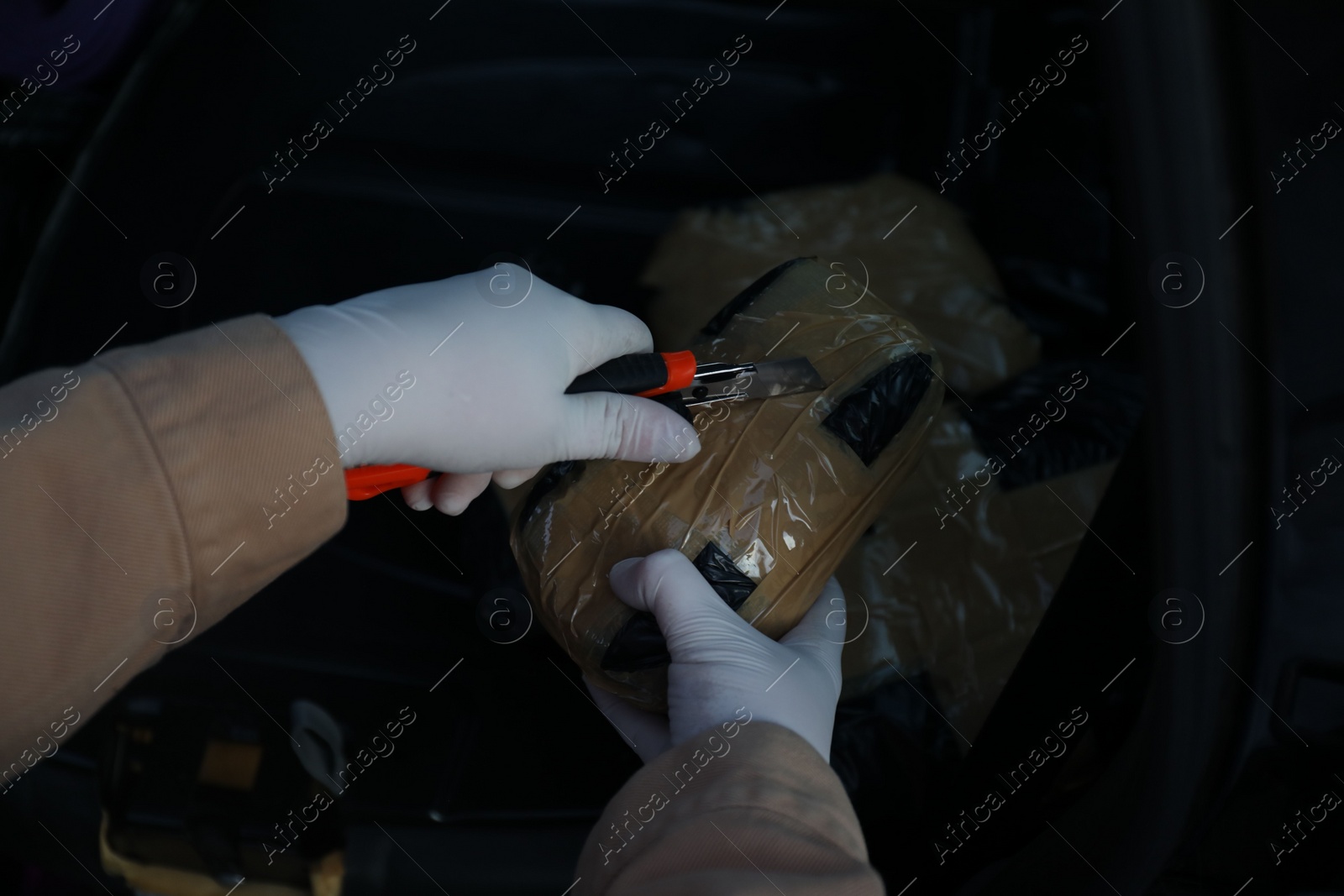 Photo of Man opening package of narcotics with stationery knife on dark background, closeup. Space for text