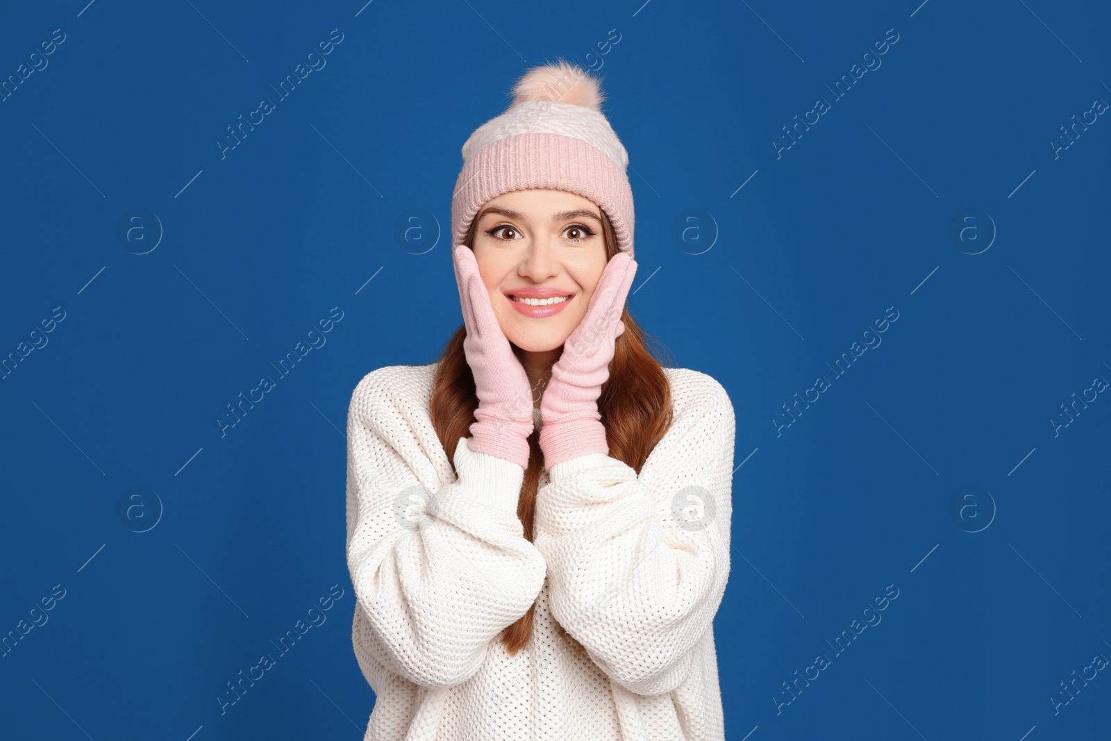 Photo of Young woman wearing warm sweater, gloves and hat on blue background. Winter season