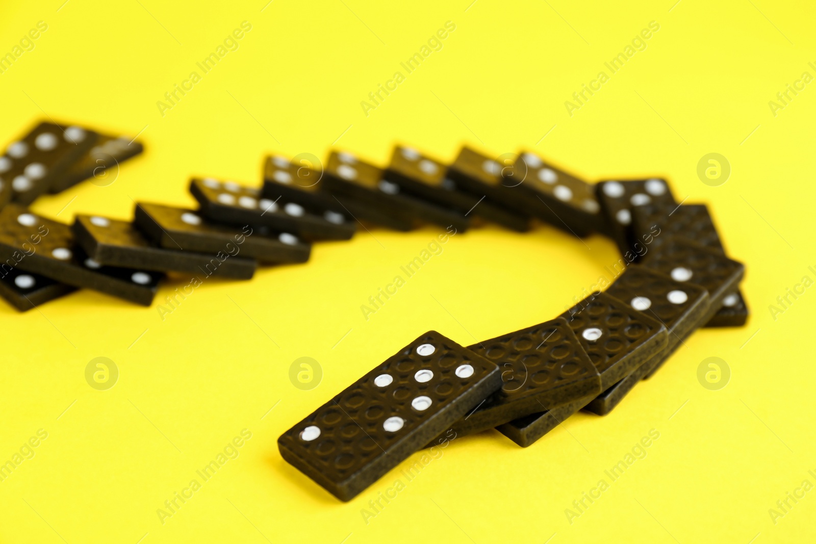 Photo of Falling black domino tiles on yellow background