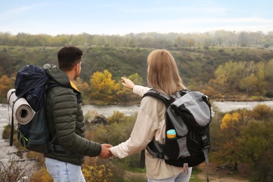 Photo of Couple of travelers with backpacks enjoying beautiful view near mountain river. Autumn vacation