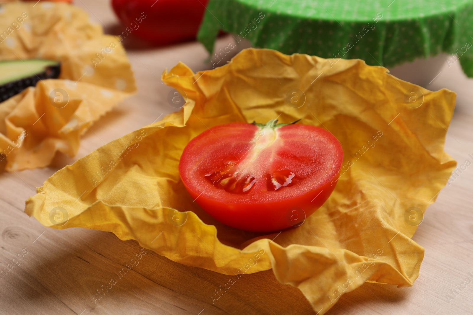 Photo of Half of fresh tomato in beeswax food wrap on wooden table, closeup