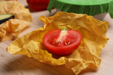 Photo of Half of fresh tomato in beeswax food wrap on wooden table, closeup