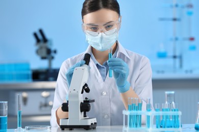 Photo of Scientist holding test tube with light blue liquid and microscope in laboratory