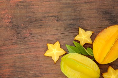 Photo of Cut and whole delicious ripe carambolas with leaves on wooden table, space for text