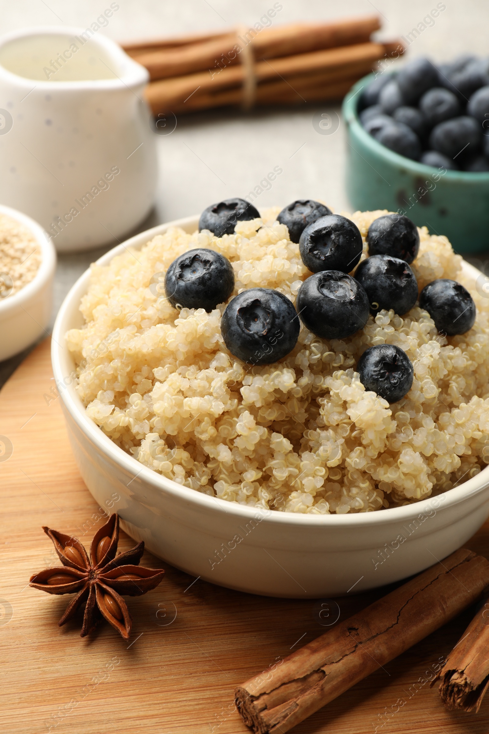 Photo of Tasty quinoa porridge with blueberries in bowl and spices on table, closeup