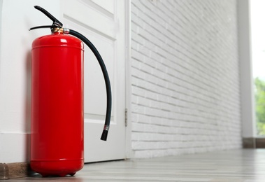 Photo of Fire extinguisher on floor near door indoors, space for text