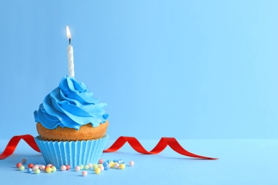 Delicious birthday cupcake with candle on color background